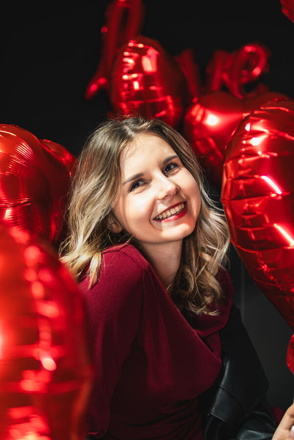 Portret Studio Walentynki Uśmiechnięta kobieta na tle czerwonych balonów w kształcie serc podczas sesji portretowej.