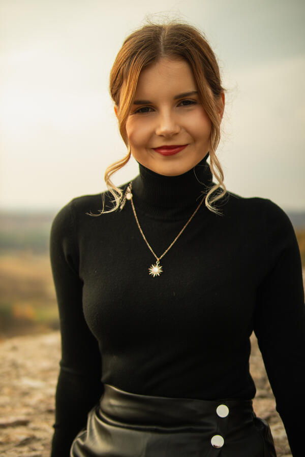 Naturalny portret kobiecy w plenerze Zbliżenie uśmiechniętej kobiety w czarnym golfie na tle rozmytego krajobrazu.